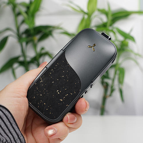 Hand holding an AirVape Legacy Pro 2 vaporizer with blurred green plant background.