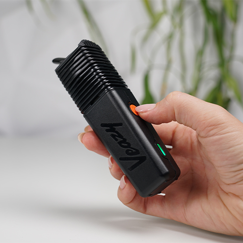 Hand pressing the orange button on a Veazy vaporizer with a green indicator light.