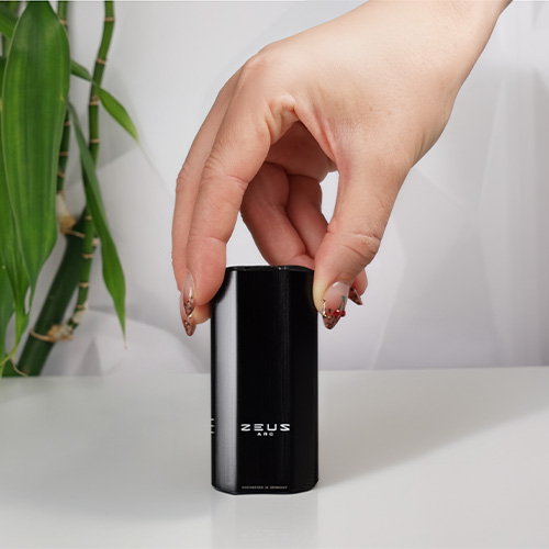 Hand holding the top of a Zeus Arc S2 vaporizer standing on a white surface.