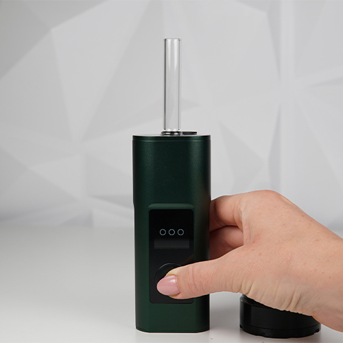 Hand pressing the control button on a Arizer Solo 3 fitted with a clear glass aroma tube.